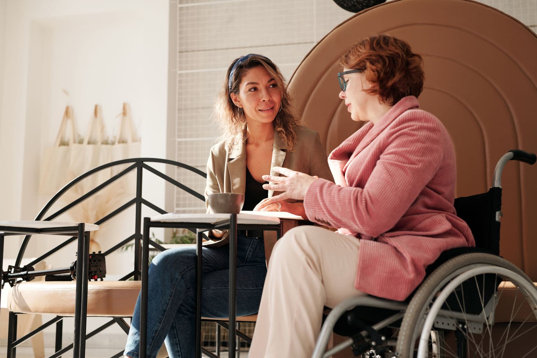 A wheelchair user and another woman having a conversation around a table